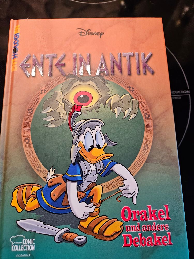 Ein gebundenes Donald Duck Buch.
Auf dem Einband steht: 
Ente in Antik, Orakel und andere Debakel