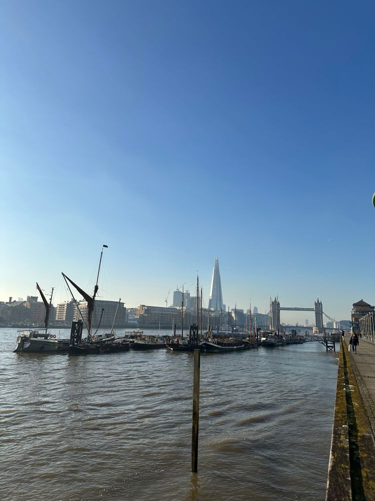 A view down the Thames. Tower bridge and the shard can be seen, with some barges and boats in the foreground 