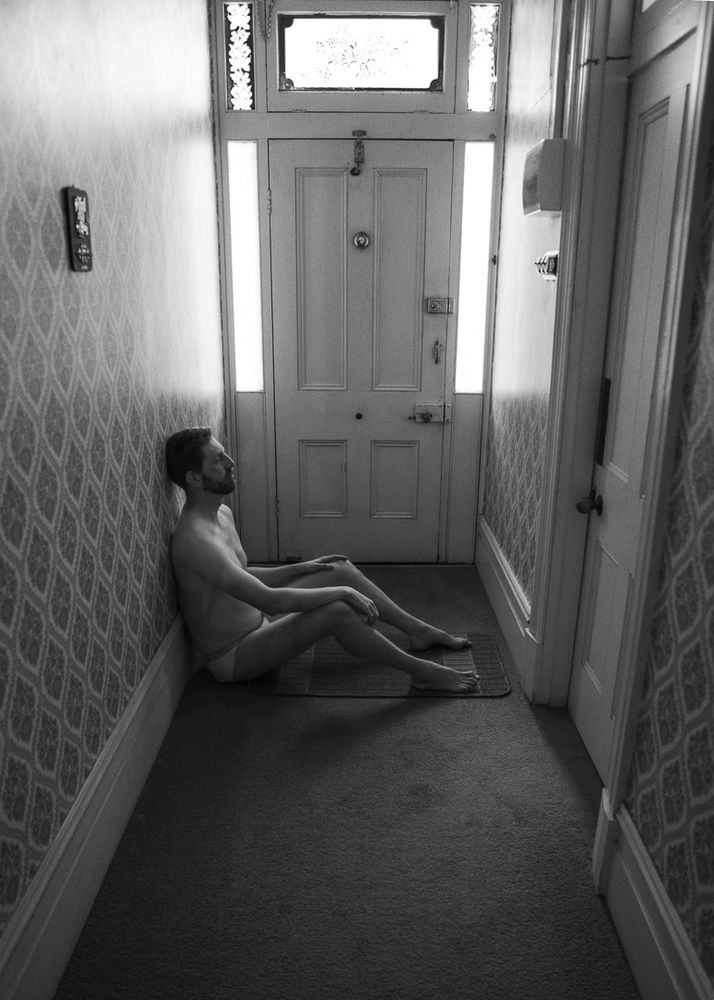 This black and white, monochrome image captures a sad yet relaxed man sitting in contemplation, dressed in pajamas, leaning against the wall. It's a reflective and quiet moment that speaks volumes.