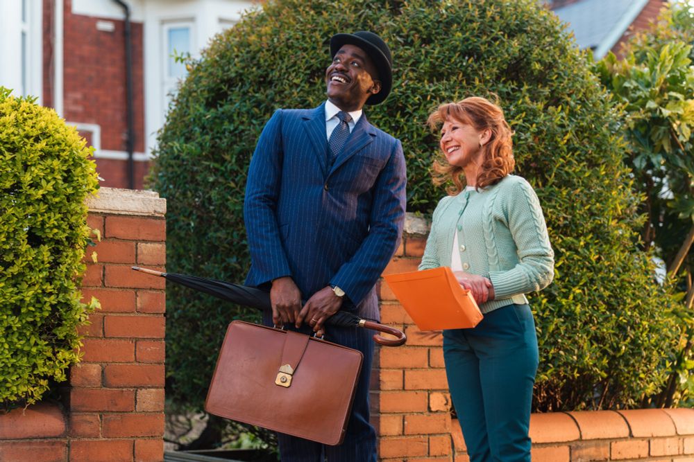 The Doctor meets his neighbor Melanie Bush in front of their peaceful home. Both looking up towards the sky, fascinated by what they see there. The Doctor looks like he is off to work, briefcase in his hands and a bowler hat on his head. Mel looks like she just did some chores in front of her house.