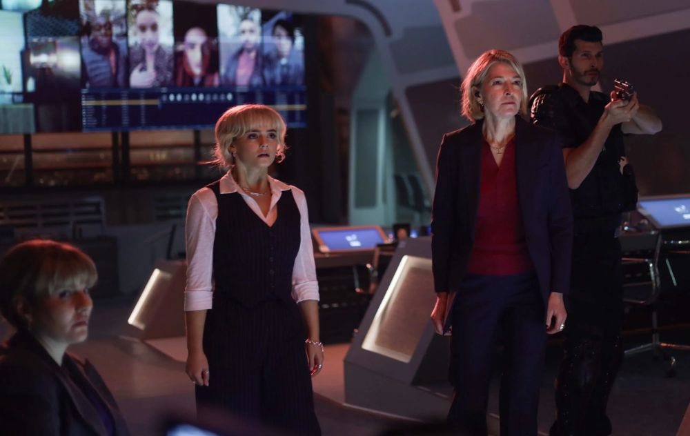 Shirley Bingham, Ruby Sunday, Kate Lethbridge-Stewart and Colonel Christofer Ibrahim standing in Unit HQ, facing something terrifying out of frame, the Colonel holding a weapon presumably aiming towards it.
In the background on  the big screen, there are multiple social media style pictures or screenshots of people talking to the camera.