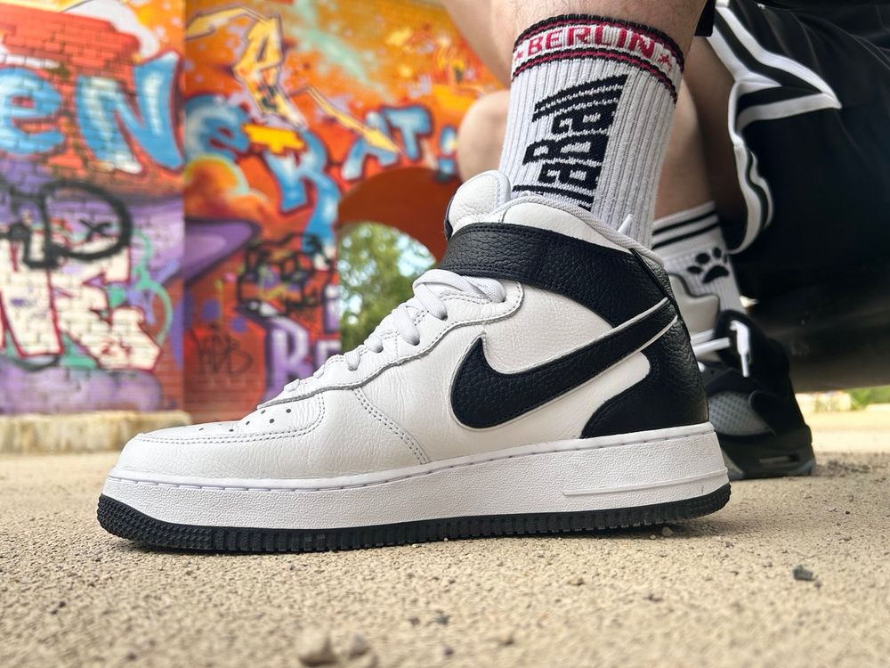 A photograph of a white high top Nike AirForce1 on a dragon paw. In the background, a wall that is completely sprayed with graffiti.