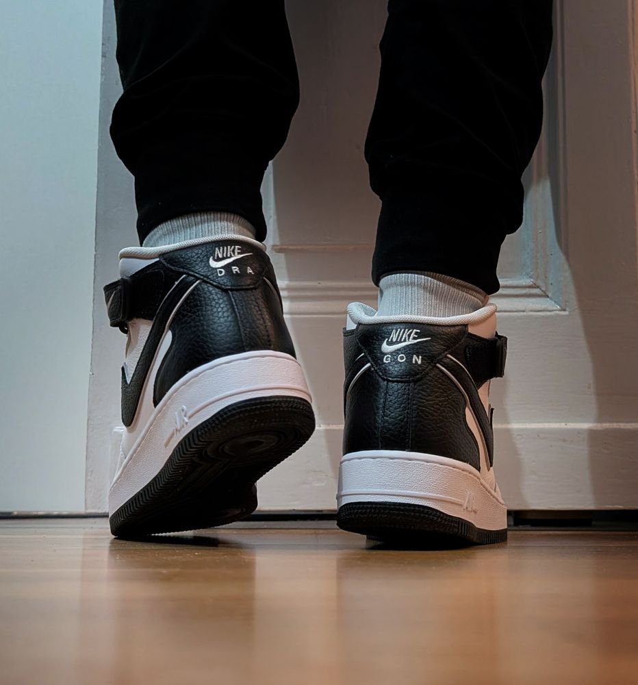 Dragon paws from behind with some mid black and white AirForce1's on. The letters DRA are written on the left and GON  are written on the right heel.