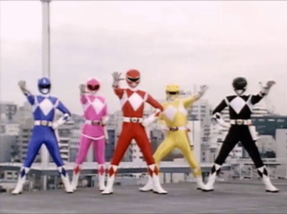 a group of power rangers are standing next to each other and waving their hands in the air .