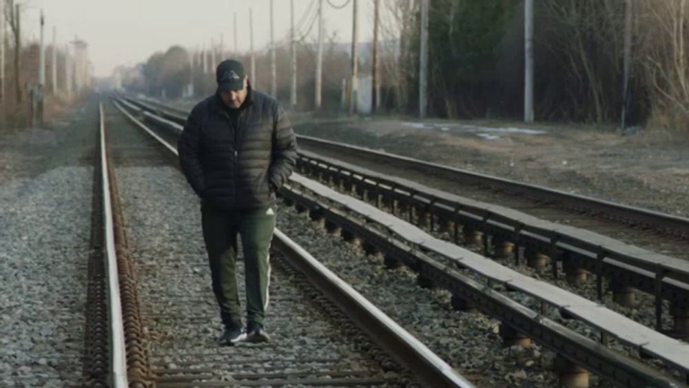 a man wearing a black jacket and a black hat walks along train tracks