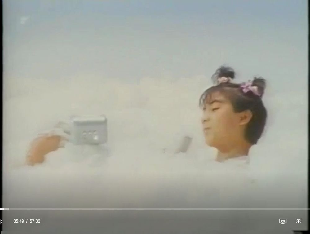 Still-image from the 1988 Japanese tokusatsu film "Star Virgin". A girl with hair buns and pink bows relaxes in a bubble bath, holding a voice recorder in her hand.