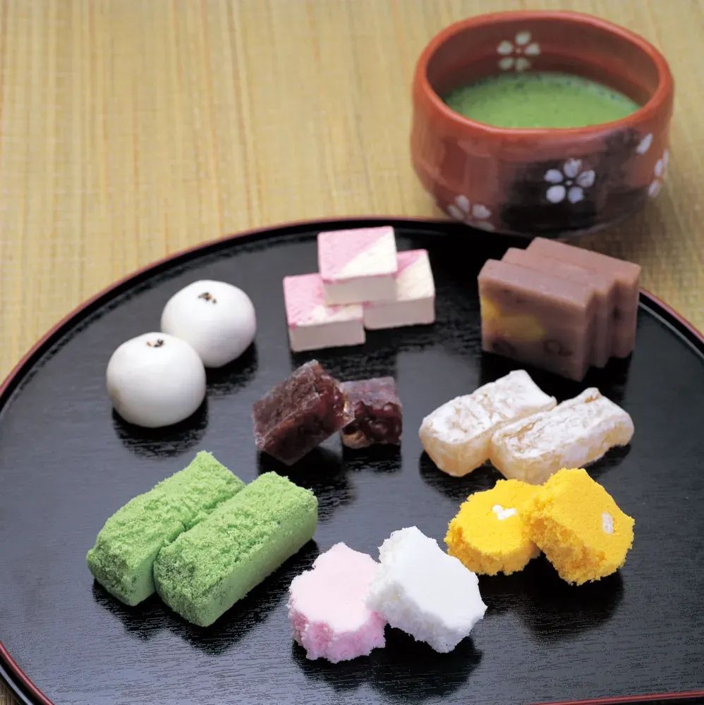 Assorted wagashi confections arranged on a black lacquered plate with matcha tea in a ceramic bowl. © Shimane Prefectural Government