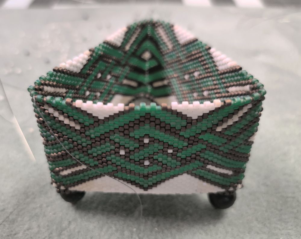 Beaded triangular shaped box with a Celtic style weave on the sides. Made with teeny tiny 11/0 delica beads in green, dark bronze and white colors.