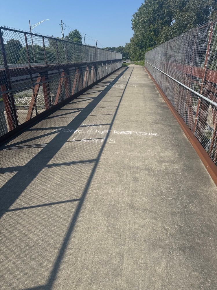 A trail crossing over an interstate highway.  Chalk graffiti says “No Concentration Camps”. 