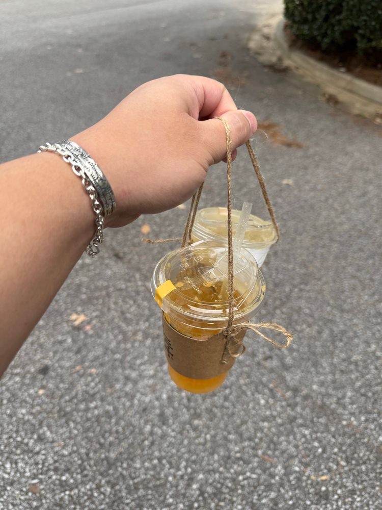 A hand holding two cups of tea using rope cup holders. 