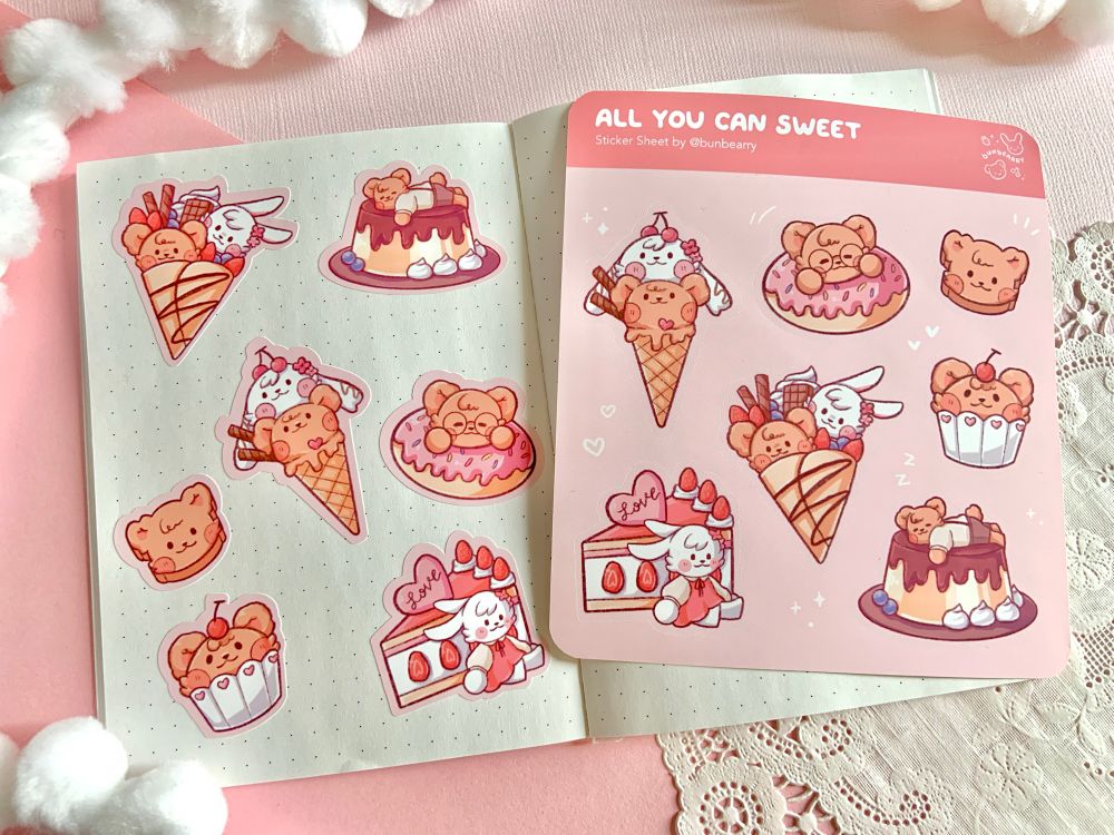 Sticker sheet and stickers on a mini notebook. The sticker sheet is titled “All You Can Sweet” and has bear and rabbit themed sweets