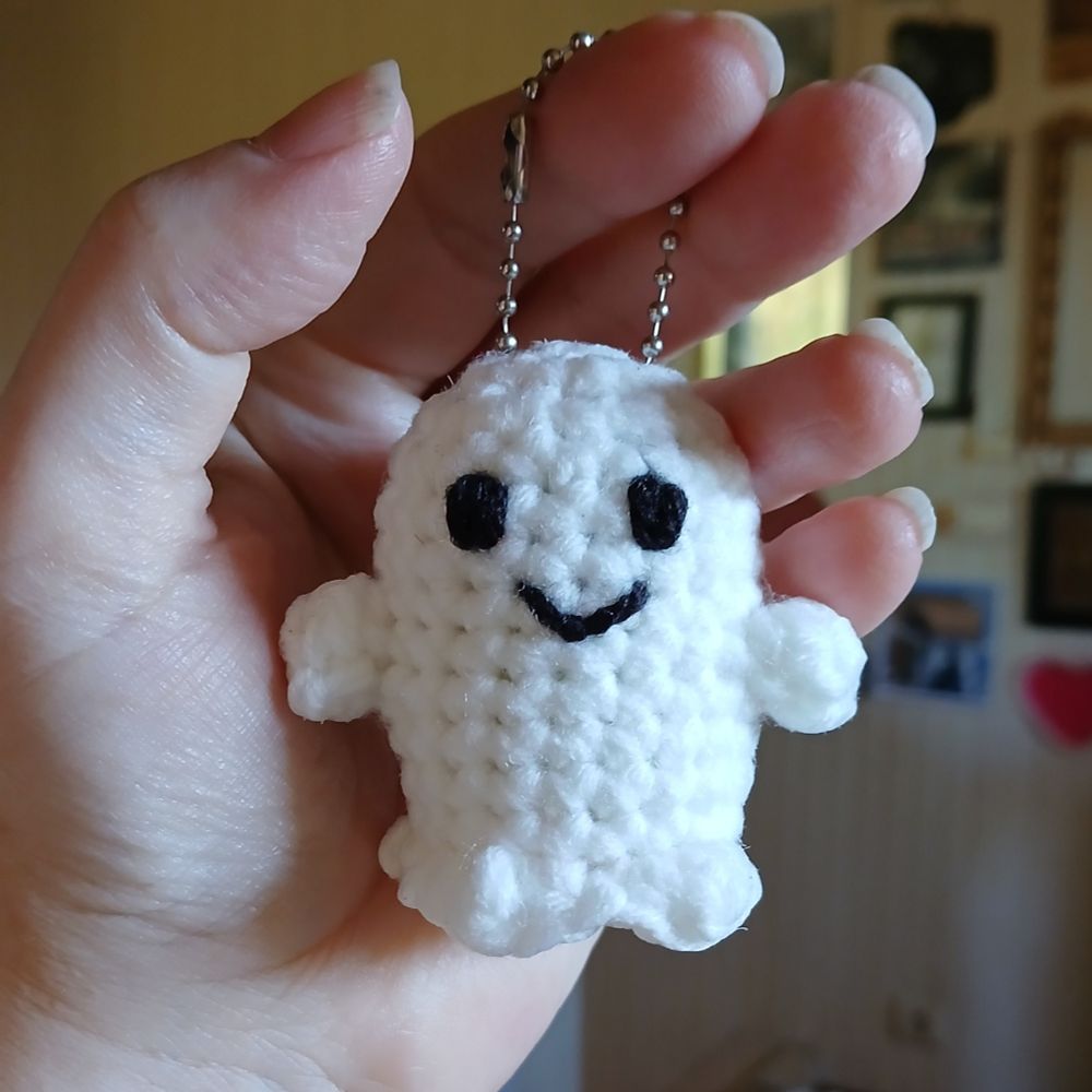 A woman's hand holding a little smiling crocheted ghost