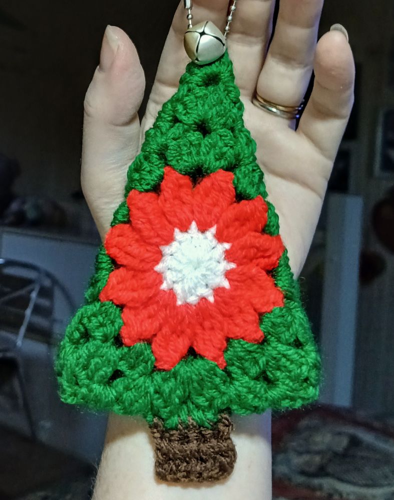 A woman's hand holding a small crocheted Christmas tree with a poinsettia in the center
