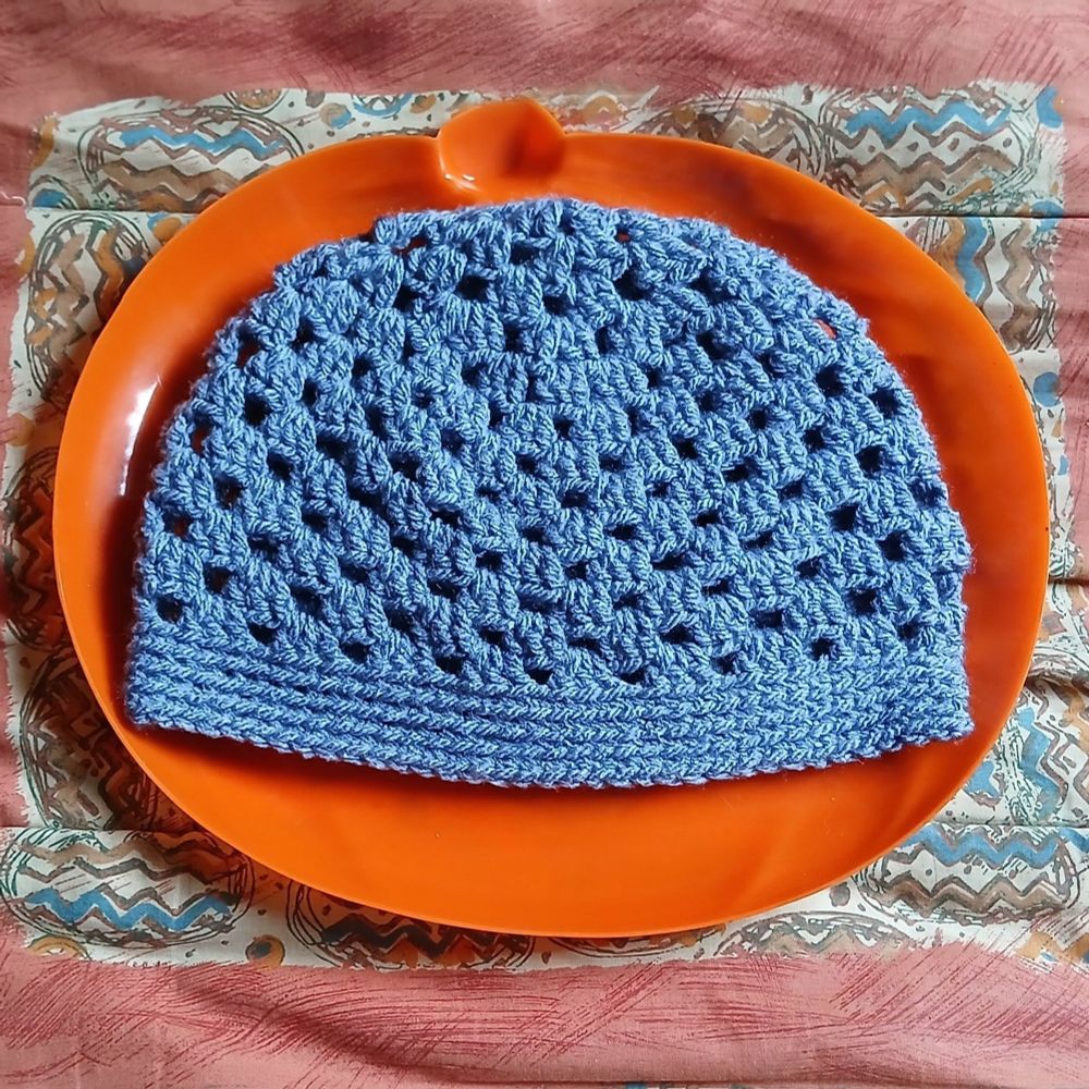 A blue crocheted hat on an orange pumpkin shaped tray