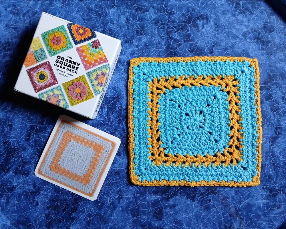 A box labeled "GRANNY SQUARE CARD DECK," a card from the deck showing a light blue and gold coloured granny square, and a crocheted granny square as depicted on the card