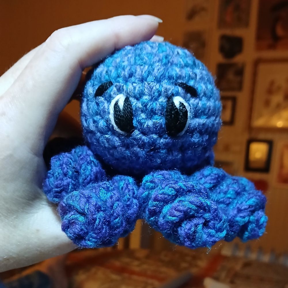 A woman's hand holding a small blue crocheted octopus
