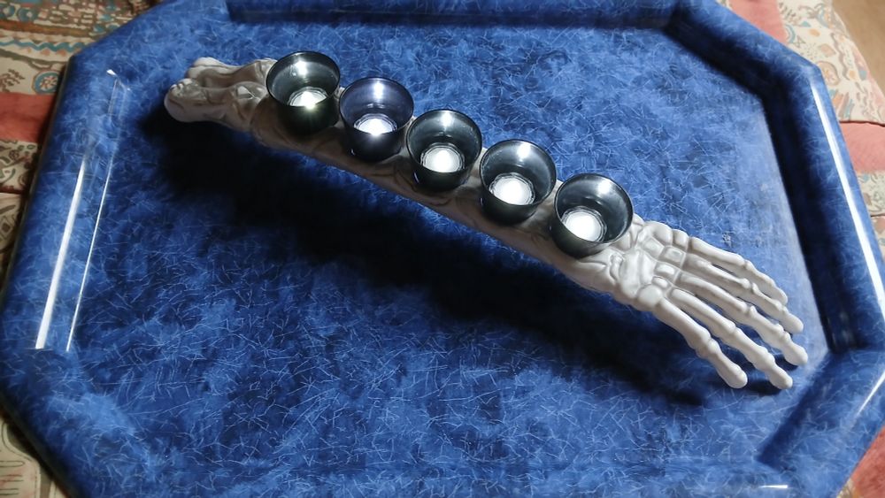 A plastic skeleton arm with 5 black cups set in it with battery operated tea lights inside