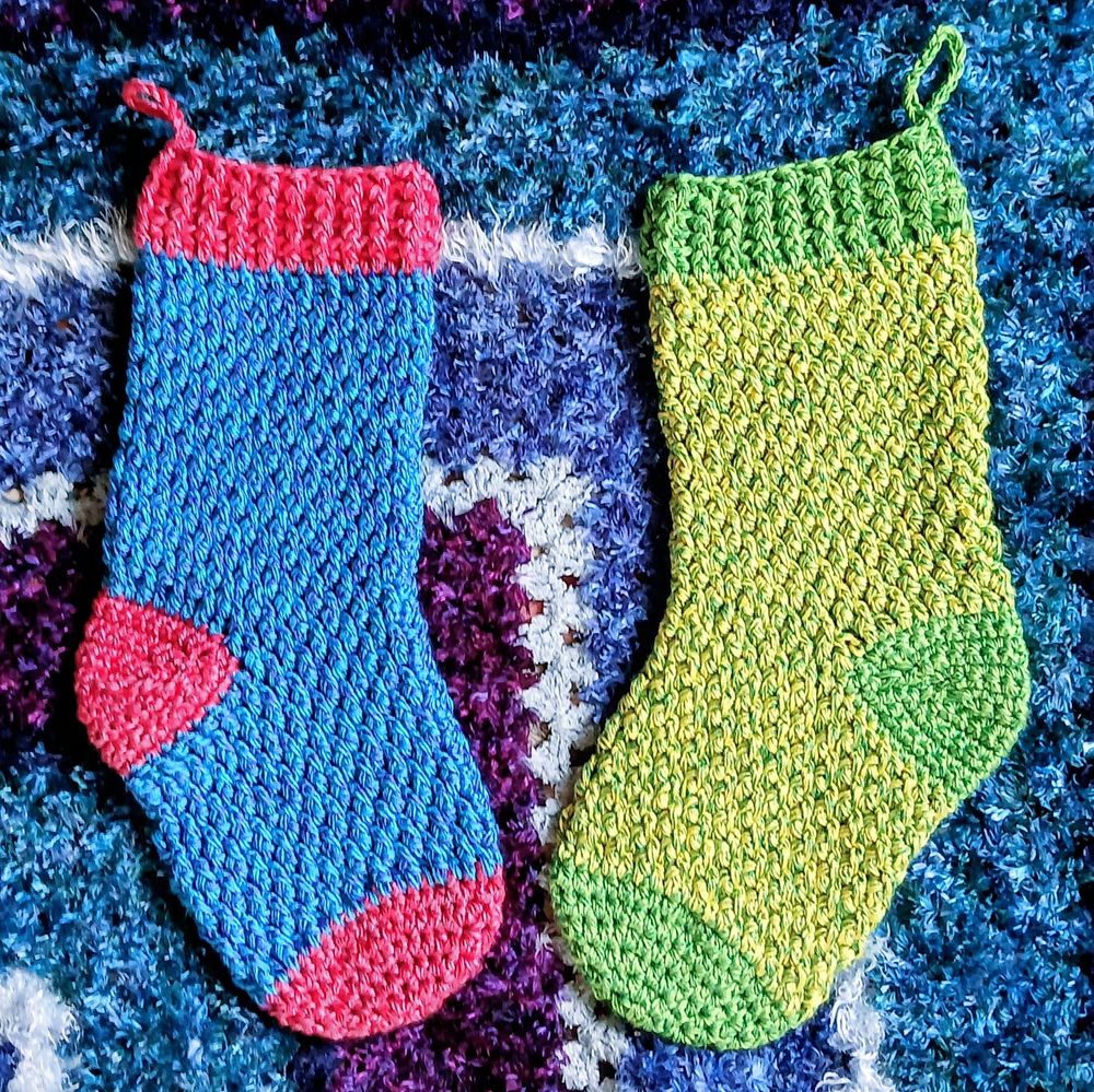 Two crocheted Christmas stockings one red and blue the other in two shades of green