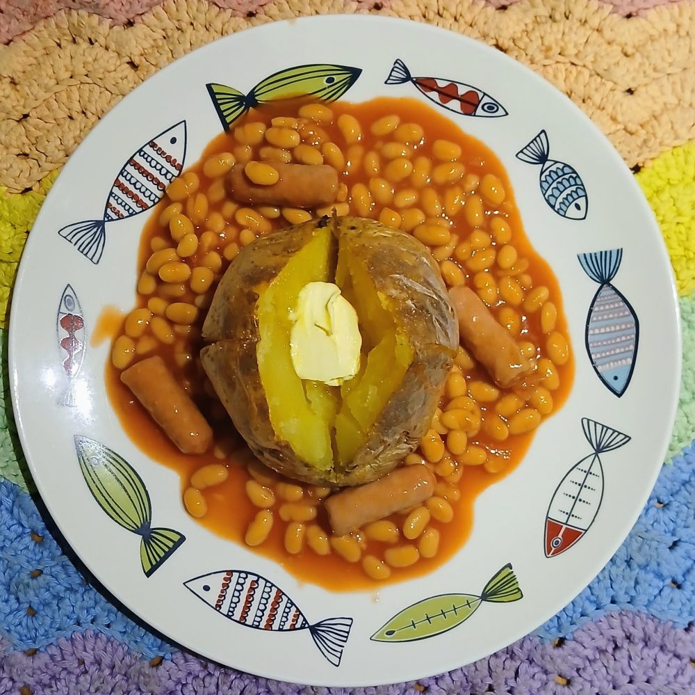 A plate with a large baked potato surrounded by sausages and baked beans