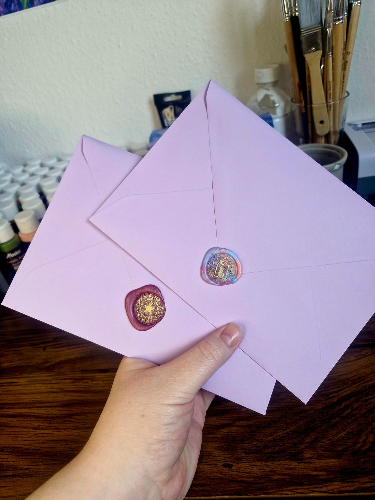 A photo of me holding two purple envelopes with one red and one rainbow wax seal