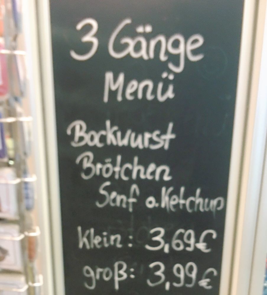 Tafel mit Kreideschrift:
3 Gänge Menü 
Bockwurst
Brötchen 
Senf oder Ketchup 
Klein 3,69€
Gross 3,99€