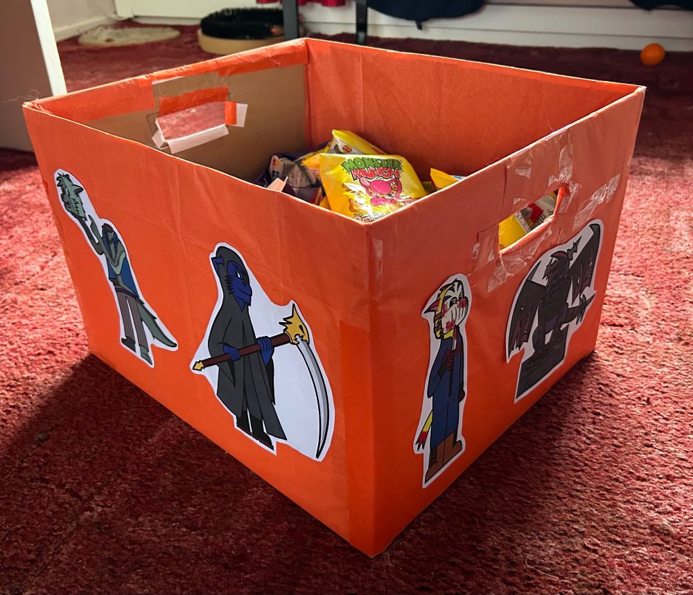 A photo of an orange box filled with candy. Drawings of anthropomorphic characters dressed as a zombie, grim reaper, slasher and gargoyle can be seen on the sides.