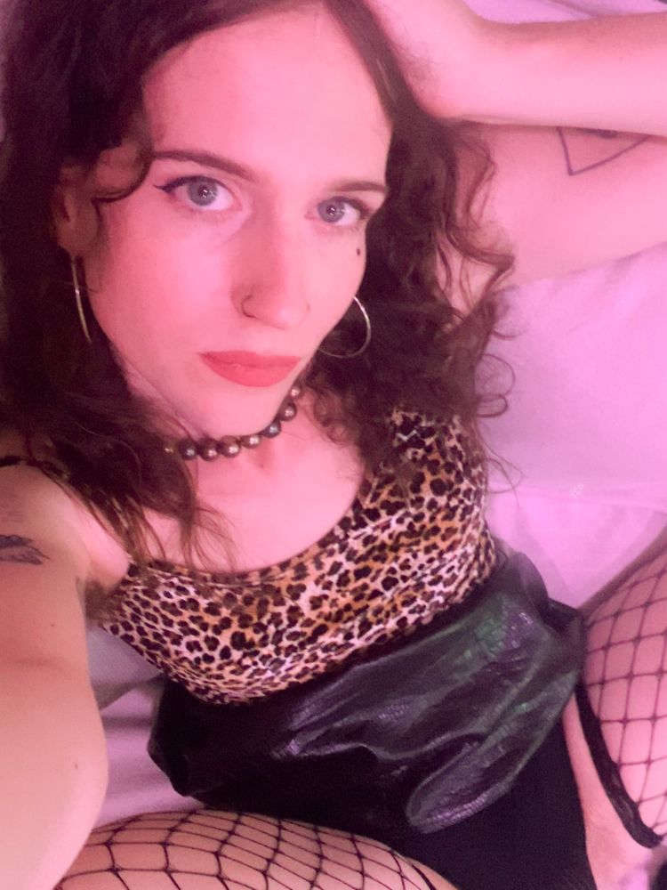Aura takes a selfie from above, she lays on her back one hand resting on her head. Her legs which have blck fishnet stockings on are spread apart. 