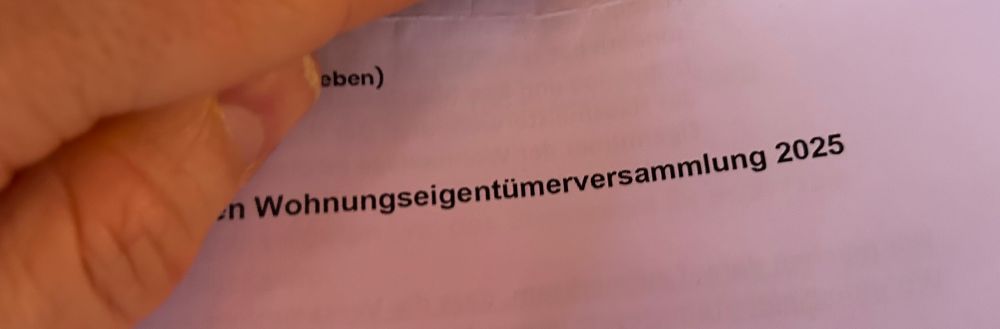 Ein Bild eines teilweise mit der Hand abgedeckten Schreiben, auf dem das Wort „Wohnungseigentümerversammlung“ zu erkennen ist. 