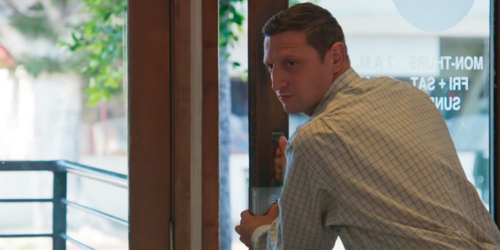 Tim Robinson pulling a push door off its hinges very slowly