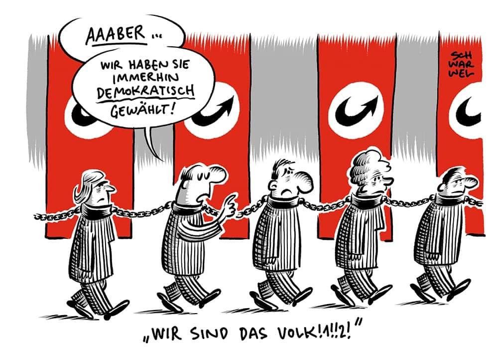 Zeichnung. Im Hintergrund rote, lang hängende Nazi-Fahnen mit AfD-Pfeil statt Hakenkreuz. Davor eine Reihe von Menschen in Sträflingskleidung, aneinander gekettet. Ein Mann sagt: „Aber wir haben sie immerhin demokratisch gewählt“