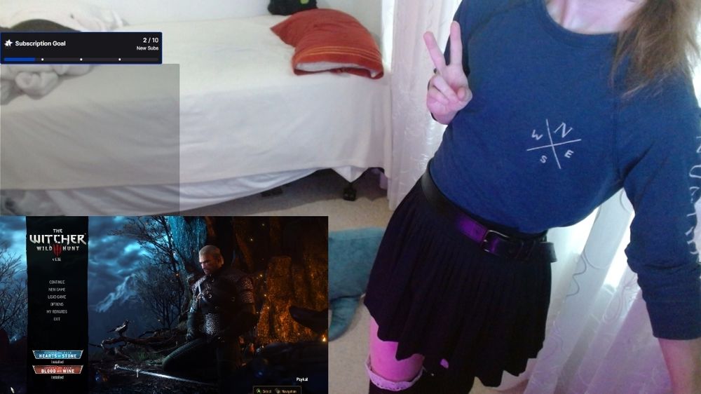 Selfie of Tmiah taken in OBS, with their game and chat overlay on left and Tmiah leaning on her desk.
