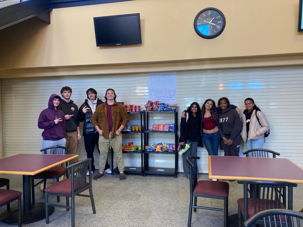 Small group of students standing next to the temporary food pantry they set up as the final project for our first year seminar 