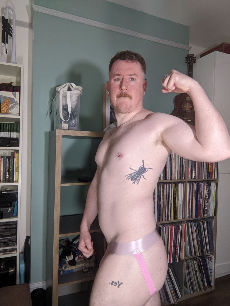 White man wearing pink jockstrap flexing bicep