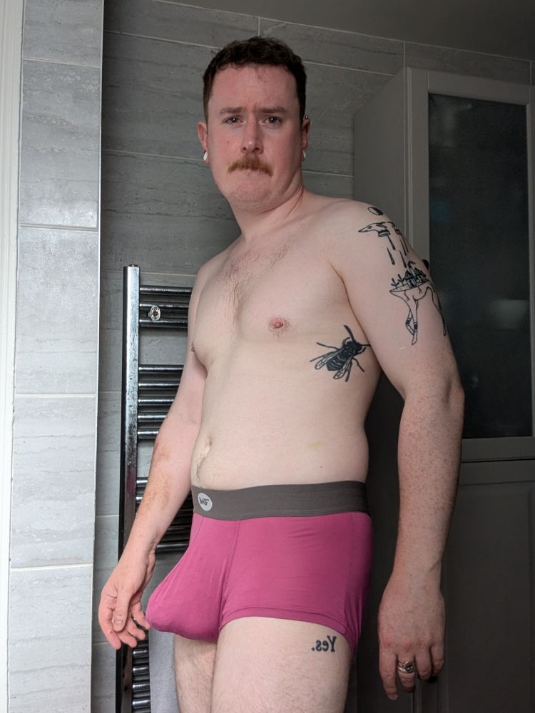 White man standing in bathroom, wearing pink boxers