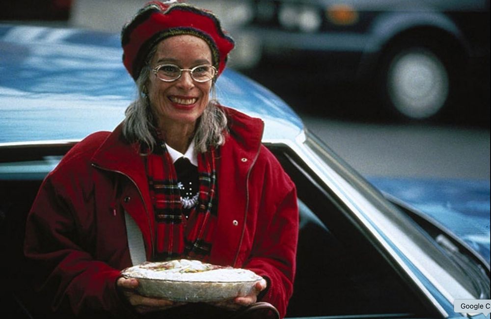 Geraldine Chaplin as Aunt Gladdy in Home for the Holidays. She wears glasses, a red coat and hat, and carries a cream pie.