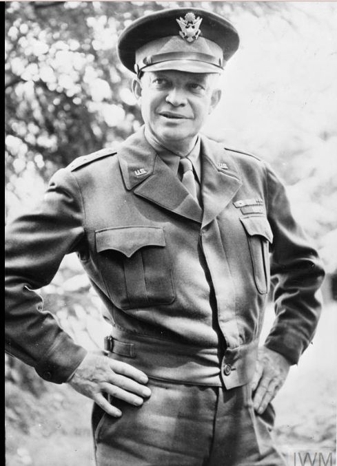 Black and white photo of Dwight Eisenhower in military uniform with his hands on his hips and a slight smile.