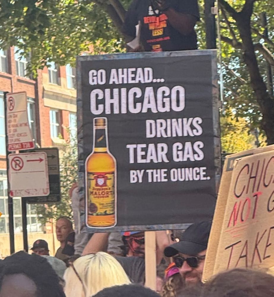 Sign at rally with picture of Malort bottle reading Go Ahead...Chicago Drinks Tear Gas By The Ounce.
