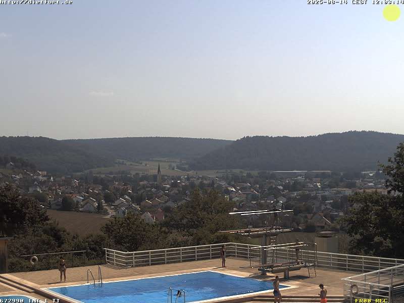 Schwimmbecken mit Sprungturm, dahinter die Stadt