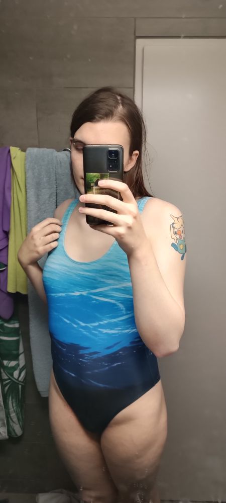 mirror selfie of a tall, brown-haired white woman in a blue one-piece swimsuit