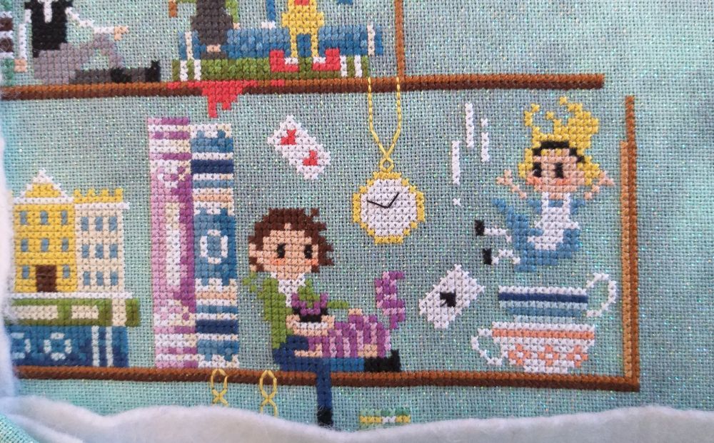 A man in a green jacket and blue pants sits beside a blue book. A purple striped cat has appeared on his lap while over his head the 2 of hearts card is floating. Beside the can is the ace of spades and a pocket watch hangs from above. To the right of them a girl in a blue dress and white apron falls into a blue striped tea cup which sits on top of a white and orange patterned tea cup.