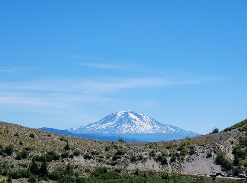 View of Mt Adams/Pahto cupped by a Ridgeline saddle. The lower mountains at its base appear blue in the summer haze.