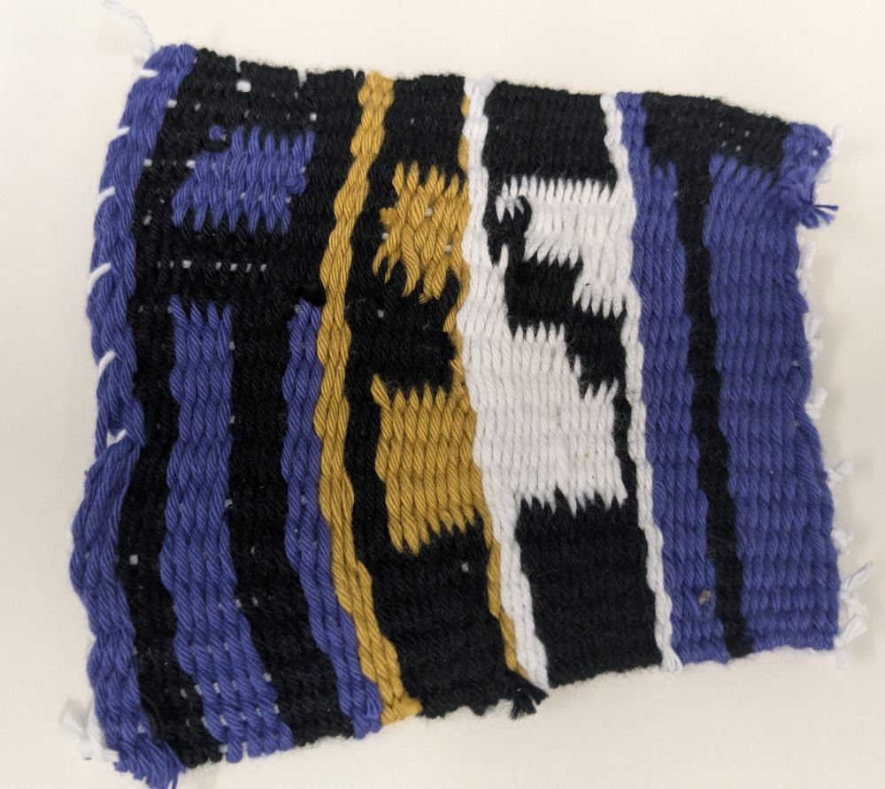 A weaving piece in the nonbinary flag colours of black, purple, white and yellow. The word REST is spelt out in black thread and in capital letters