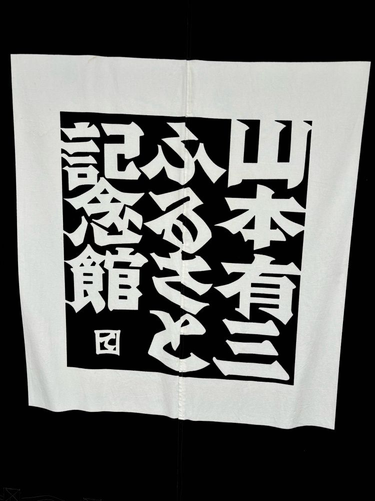 ゆぞさんのふるさと記念館の看板？垂れ幕。
黒い布に白抜きで、記念館の名前がレトロな書体で書かれており、周りをぐるっと四角い白い枠で囲っている。