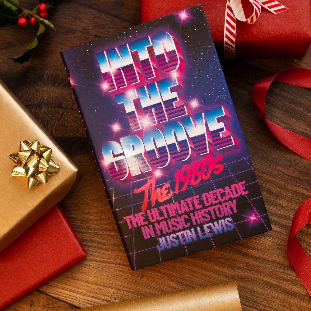 My new book, #IntoTheGroove: The 1980s - The Ultimate Decade in Music History, by me, Justin Lewis, next to some wrapped Christmas gifts and some wrapping paper. 