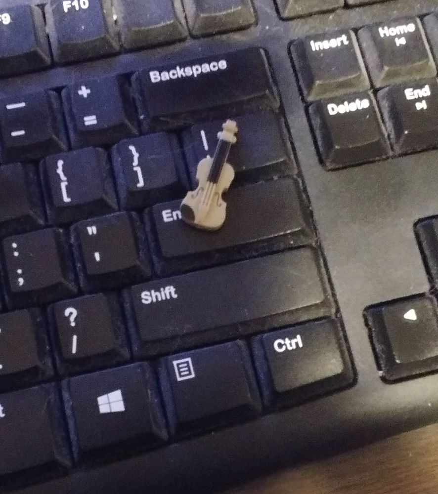 A very tiny LEGO-sized violin sits on a keyboard. It's notably smaller than the ENTER key