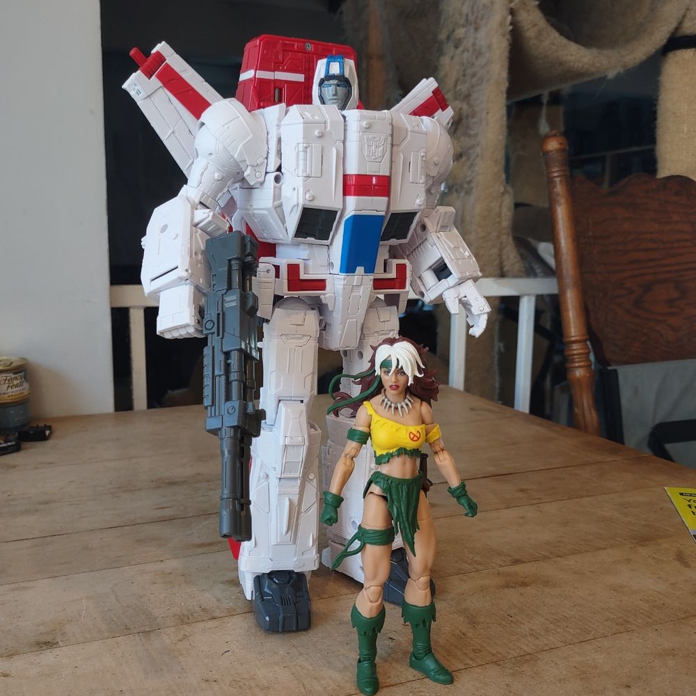 A white and red toy robot looms over a Rogue action figure.