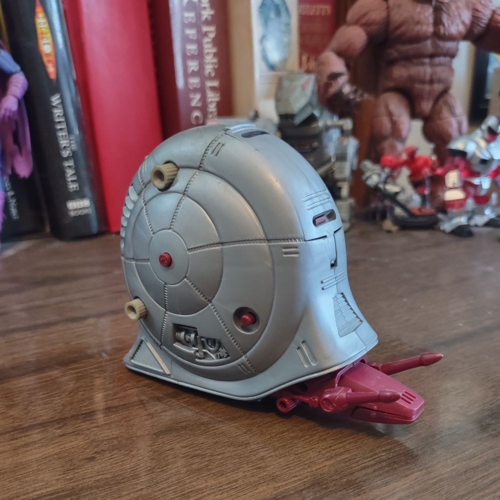 A toy mechanical snail sits on a wooden desk. Literally, a robot snail  It's got laser guns for antenna and a gunmetal gray shell.