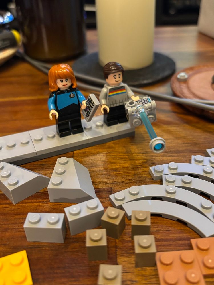 Lego minis of Wesley Crusher and Beverly Crusher behind various Lego pieces on a table.