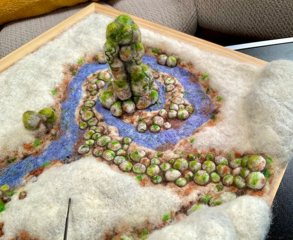 A needlefelted landscape work in progress of a waterfall, stream and standing stone