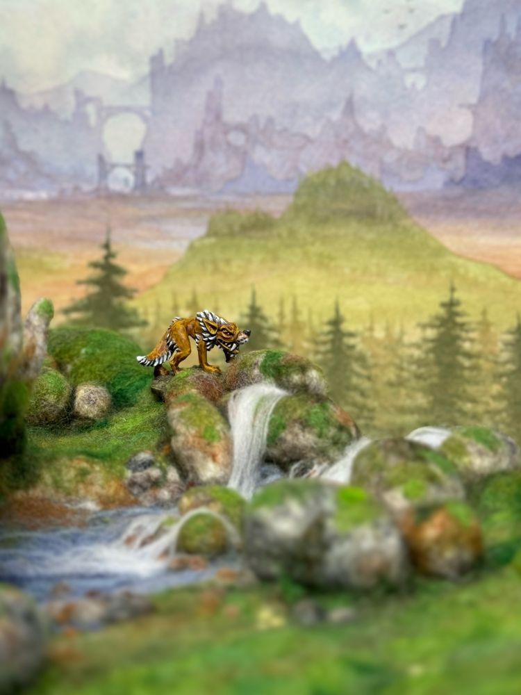 A painted wolf miniature on needle felted terrain with a waterfall and a painted landscape background.